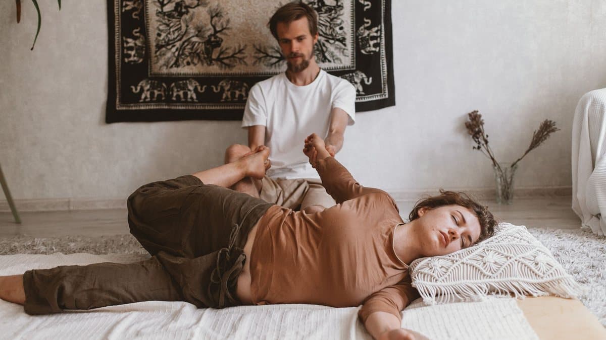 Séance de massage thaï au sol, sur un futon, le praticien étirant la jambe de la personne allongée