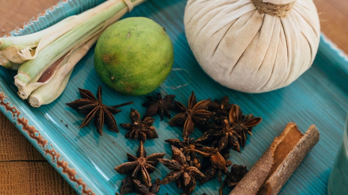 Pochon d'herbes thaï posé sur un plateau, à côté de citronnelle, d'anis étoilé et de cannelle