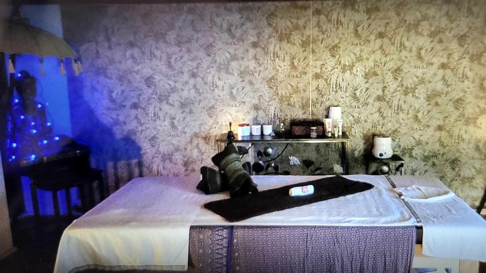 La table de massage du cabinet, drapée de tissus thaïs, devant une statue de Bouddha éclairée