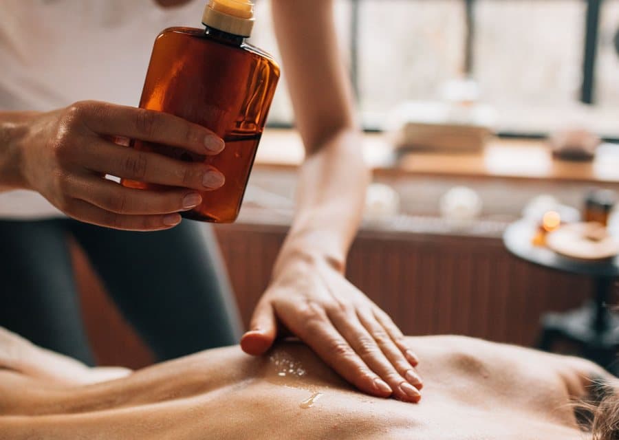 Huile de massage versée sur un dos, lors d'un soin aux huiles chaudes