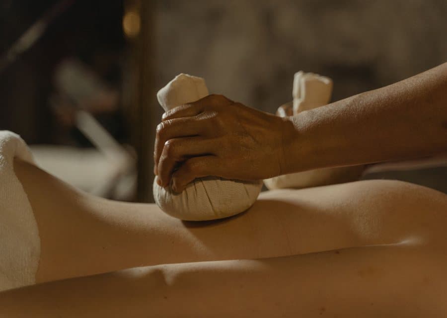 Pochon d'herbes chaudes appliqué sur le dos d'une personne allongée