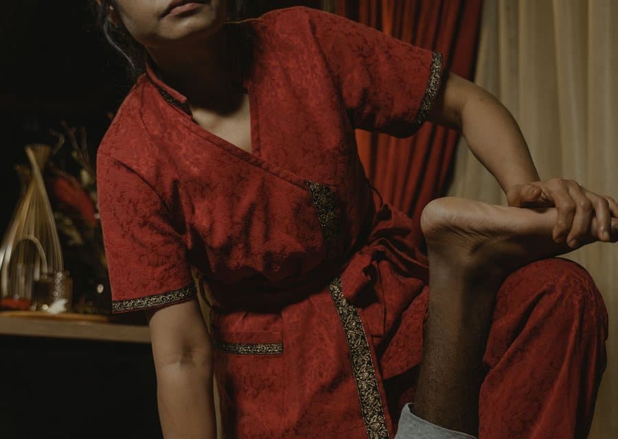 Thérapeute en tenue traditionnelle thaïe étirant la jambe d'une personne allongée